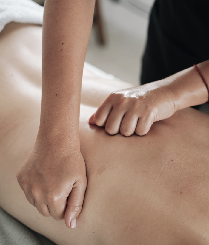 Manos de terapeuta aplican presión con nudillos en la espalda de una persona en camilla.