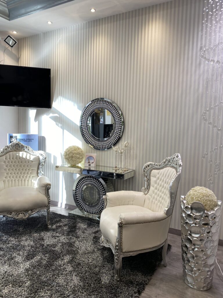 Sala de espera con dos sillones blancos capitoné, consola espejada, espejo circular y pared a rayas verticales.